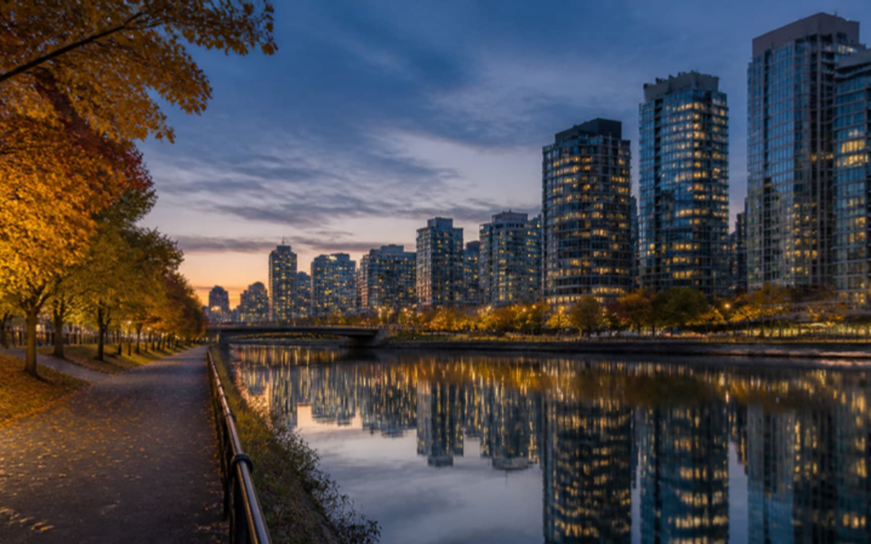 Tours de condos au crépuscule aux fenêtres éclairées, reflétées dans un plan d'eau calme, avec un sentier aux arbres dorés au premier plan — illustration générée par IA
